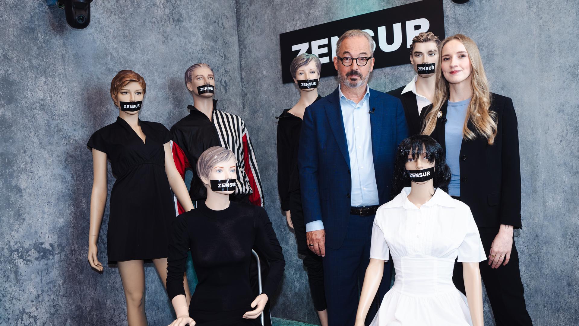 Leonie Plaar und Jan Fleischhauer sind umgeben von Schaufensterpuppen, denen je ein schwarzer Balken mit der Aufschrift "Zensur" über den Mund geklebt wurde.