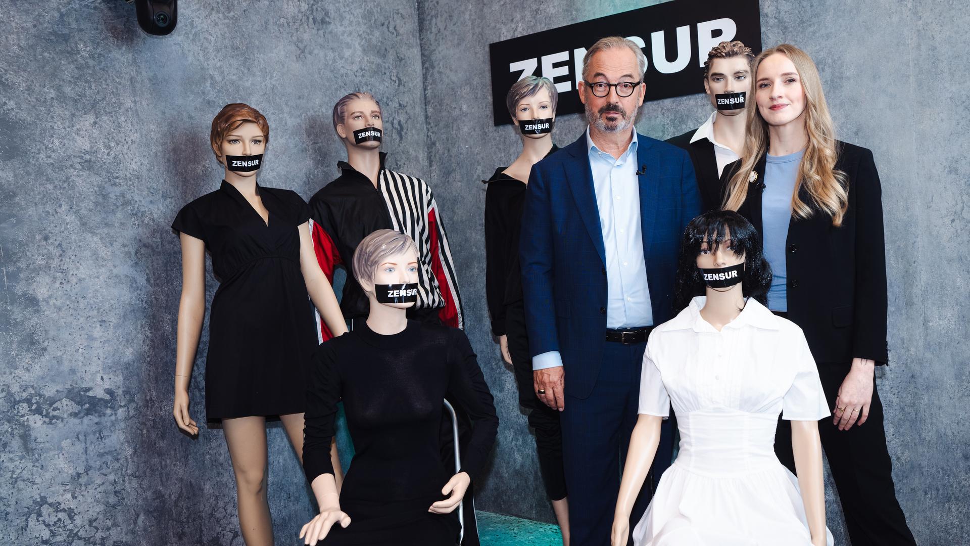 Leonie Plaar und Jan Fleischhauer sind umgeben von Schaufensterpuppen, denen je ein schwarzer Balken mit der Aufschrift "Zensur" über den Mund geklebt wurde.