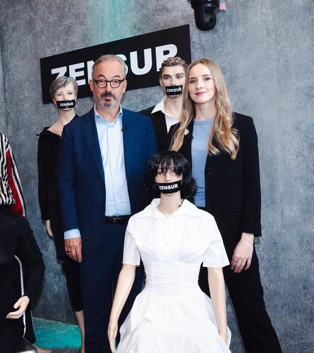 Leonie Plaar und Jan Fleischhauer sind umgeben von Schaufensterpuppen, denen je ein schwarzer Balken mit der Aufschrift "Zensur" über den Mund geklebt wurde.