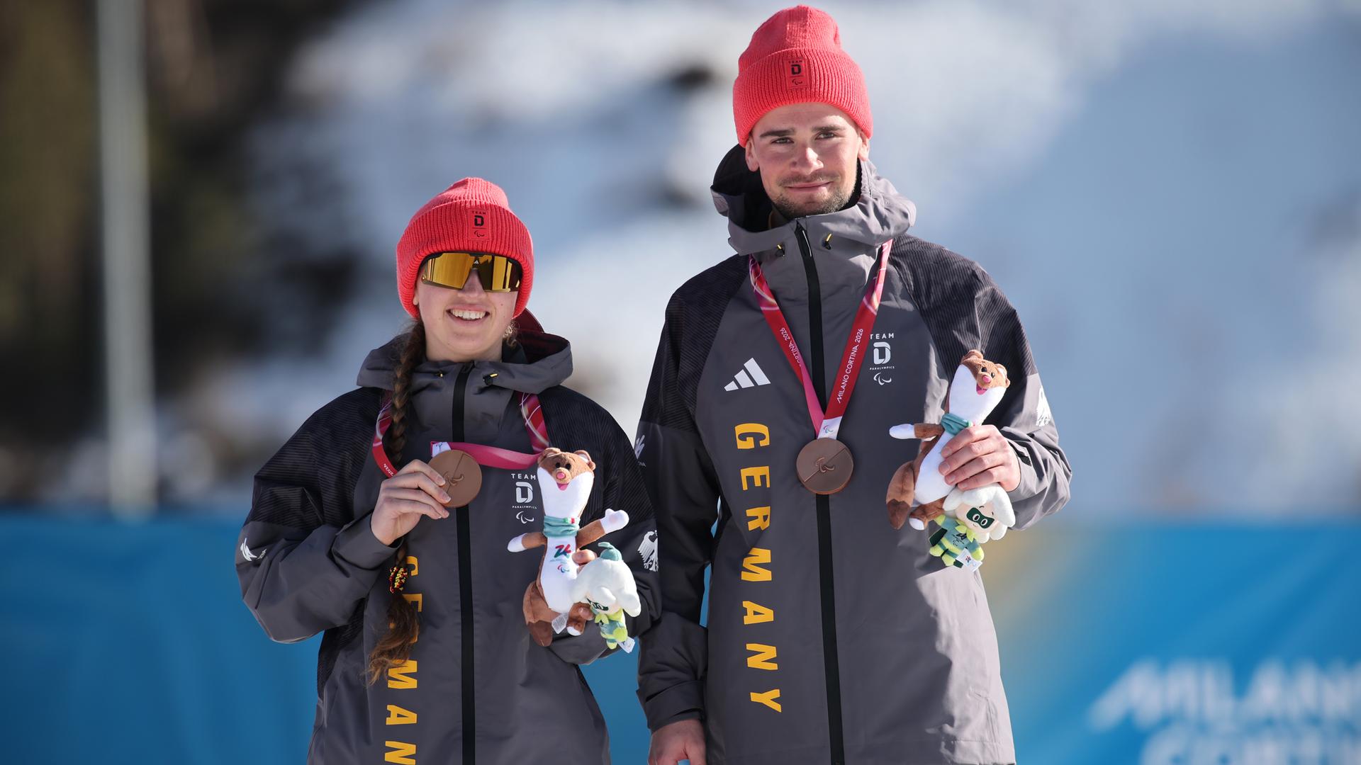 Die deutsche Biathletin und Skilangläuferin Leonie Maria Walter präsentiert freudig mit ihrem Coach Christian Krasman ihre Bronzemedaille