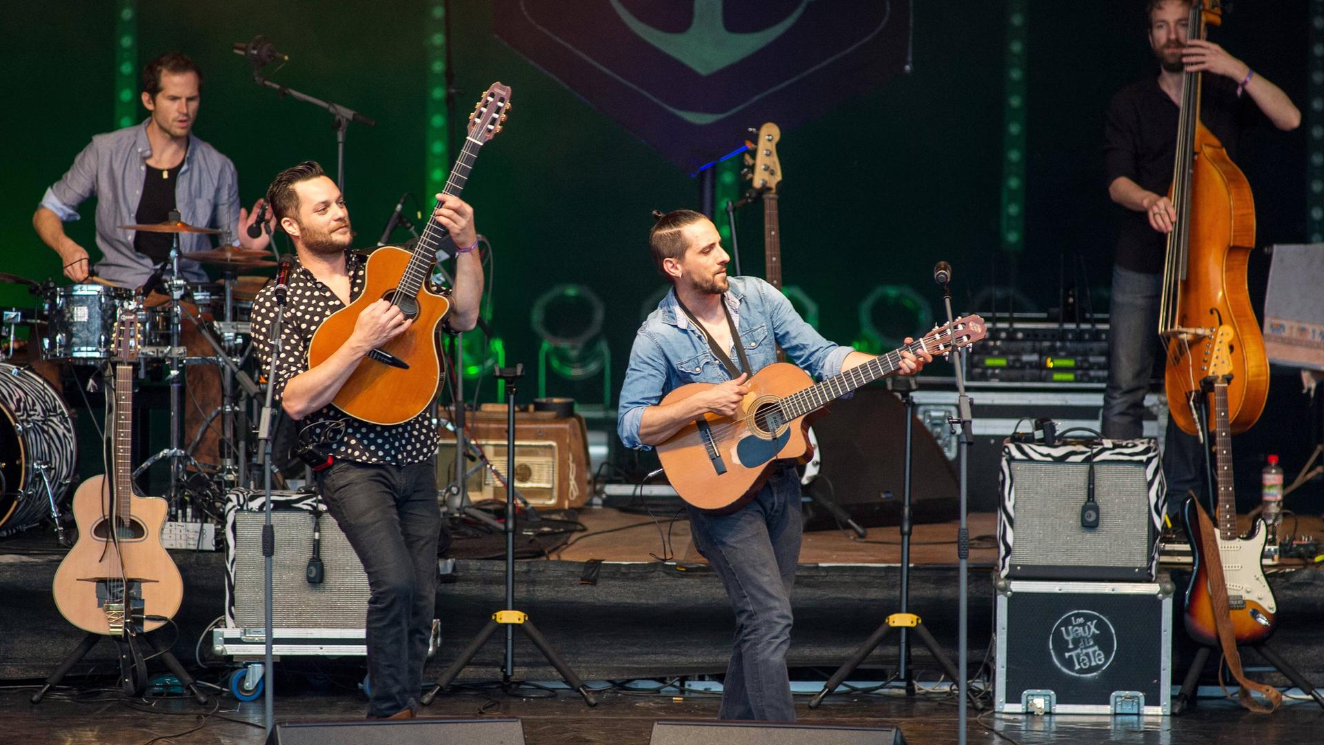 Mehrere Gitarristen und ein Bassist spielen auf einer Bühne.