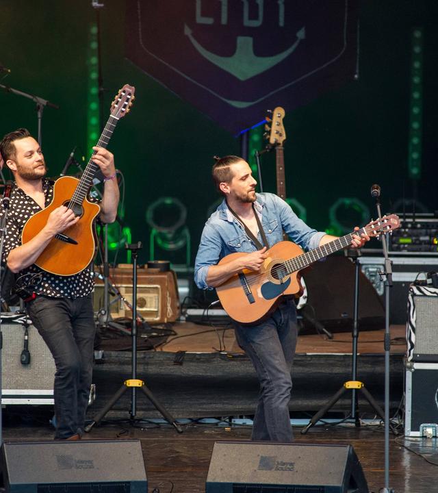 Mehrere Gitarristen und ein Bassist spielen auf einer Bühne.