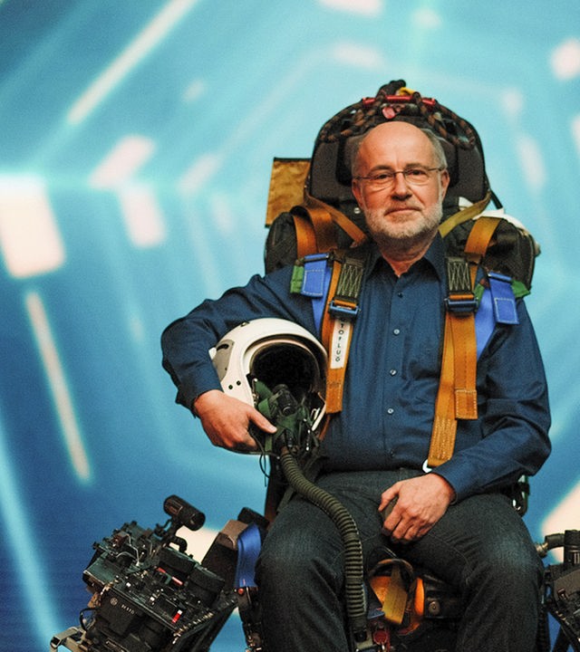 Harald Lesch sitzt auf einem Pilotensitz und schaut in die Kamera.