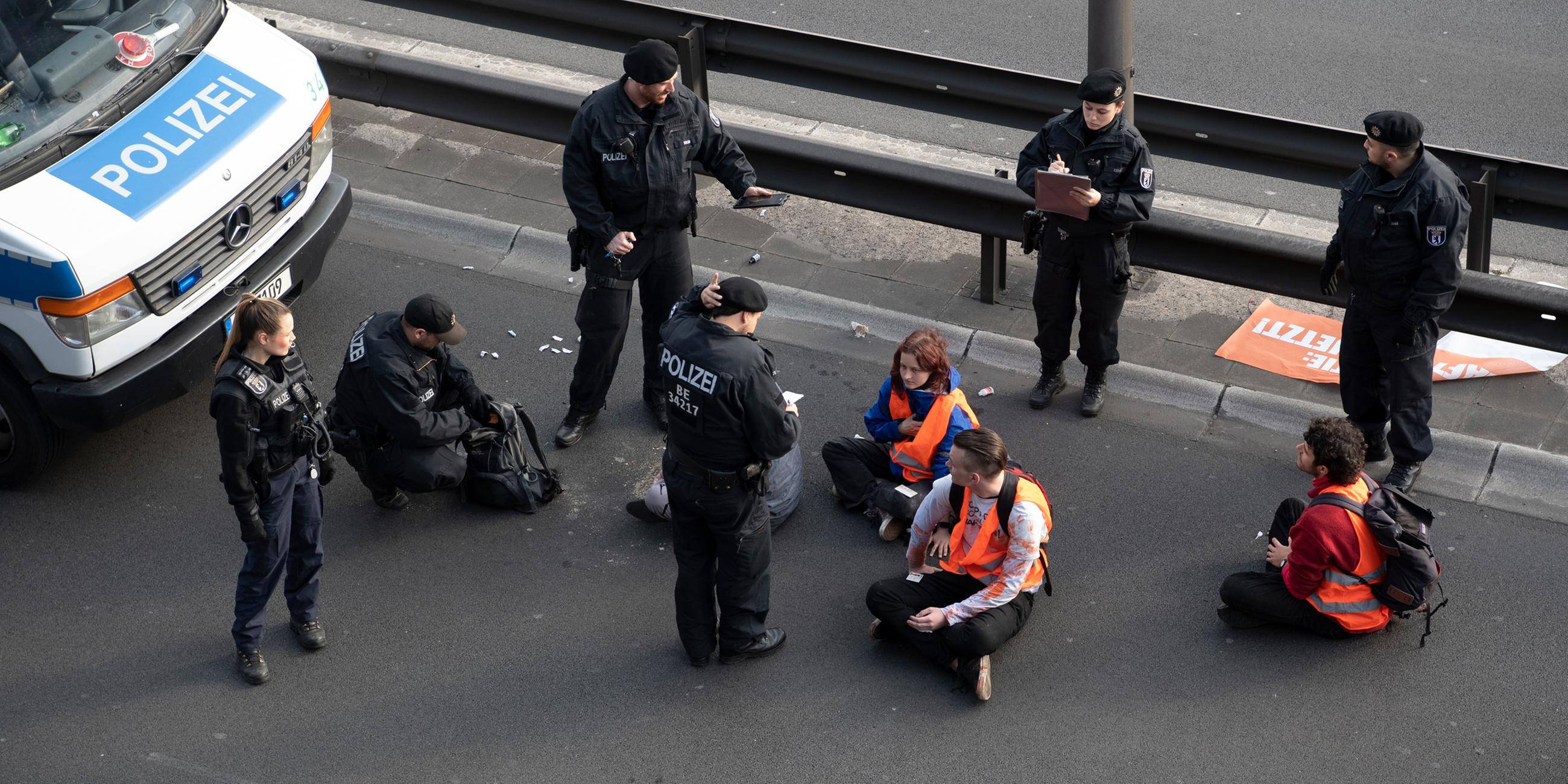 Aktivisten der "Letzten Generation" blockieren Stadtautobahn in Berlin - Polizeibeamte stehen bei der Gruppe