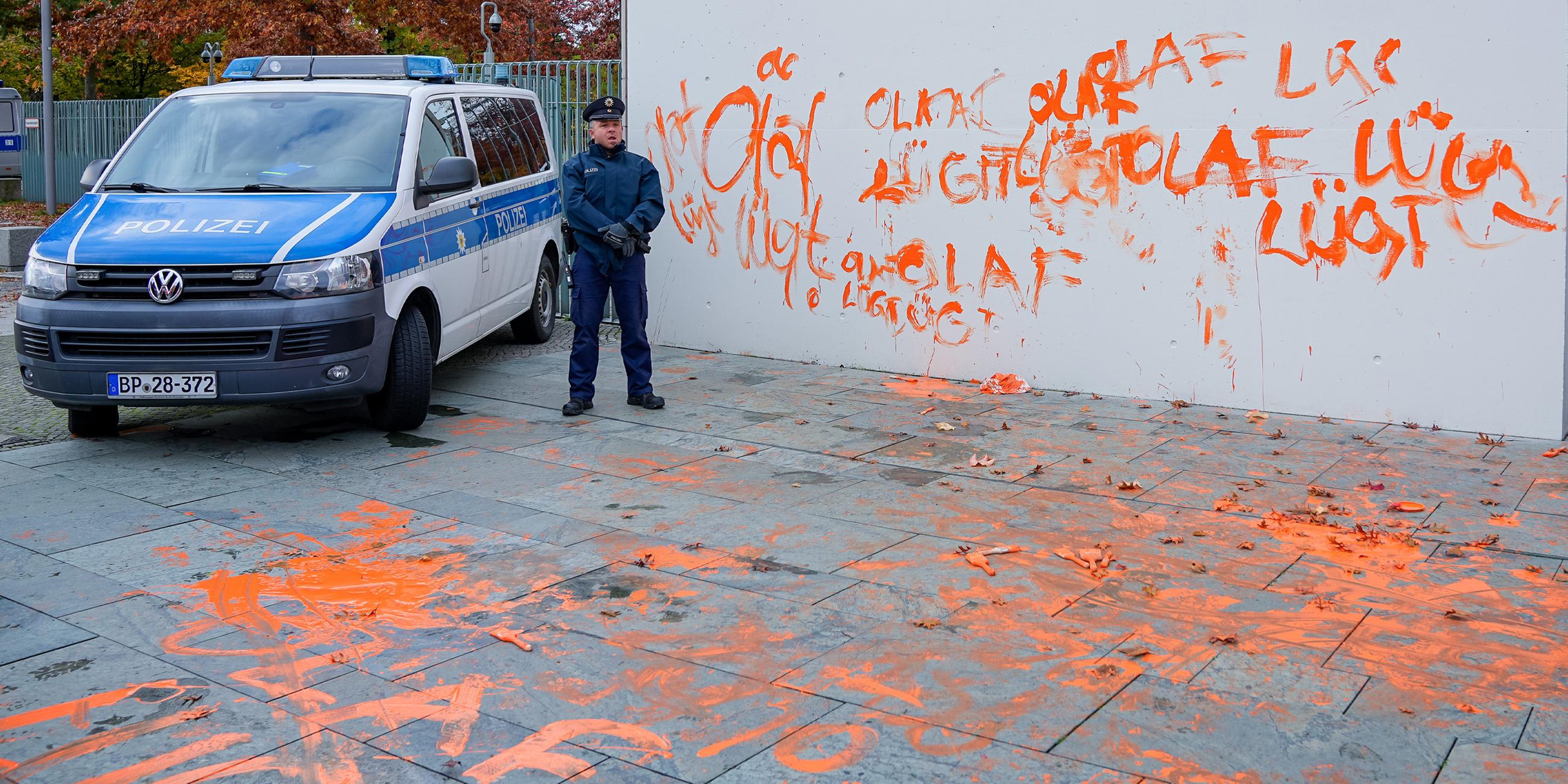Ein Polizeiwagen und ein Polizist vor dem mit Farbe beschmierten Kanzleramt und dem Boden davor. (31.10.2023)