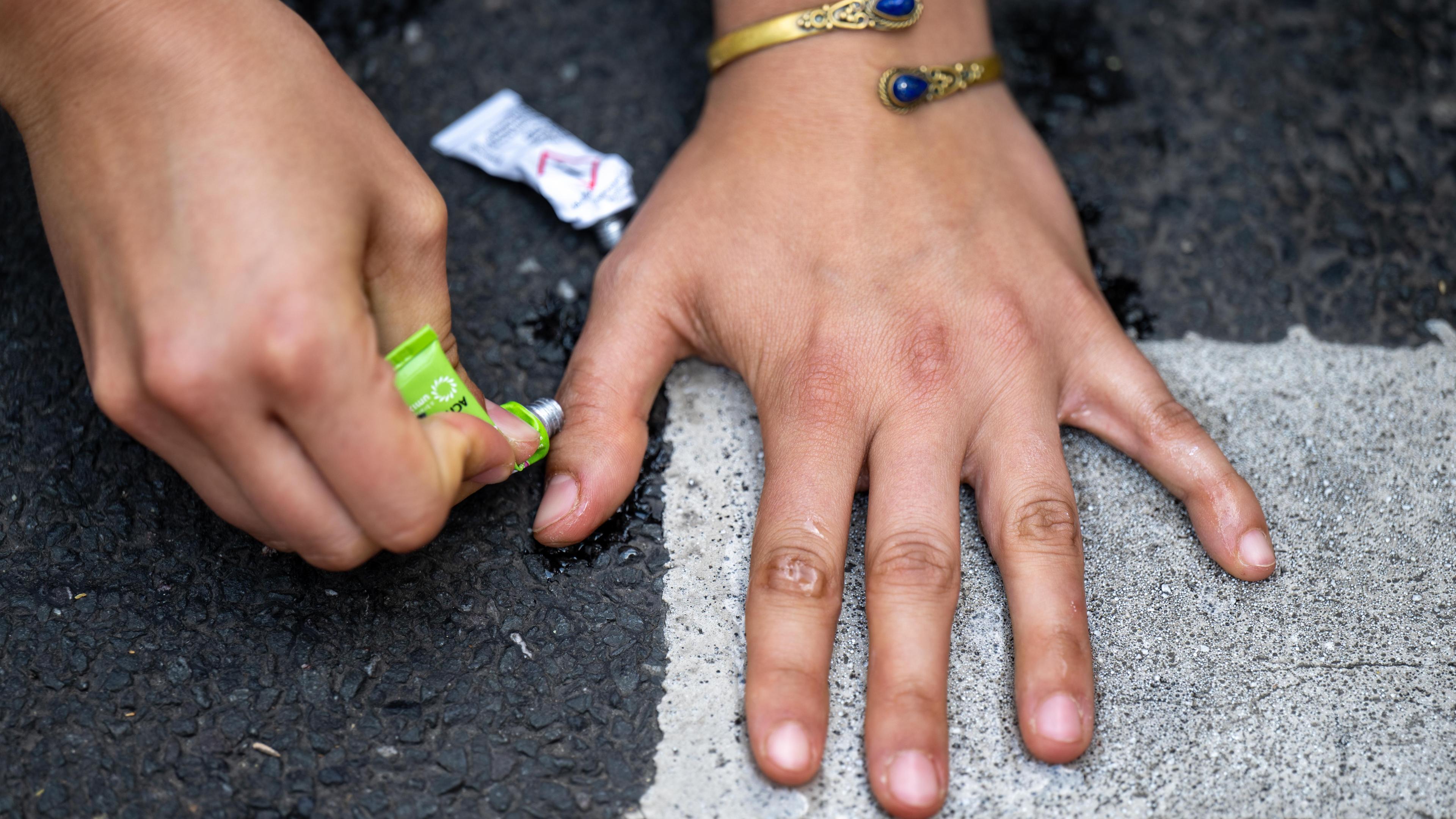 Die Hand einer Klimaaktivistin der Gruppe «Letzte Generation» klebt auf einer Straße.