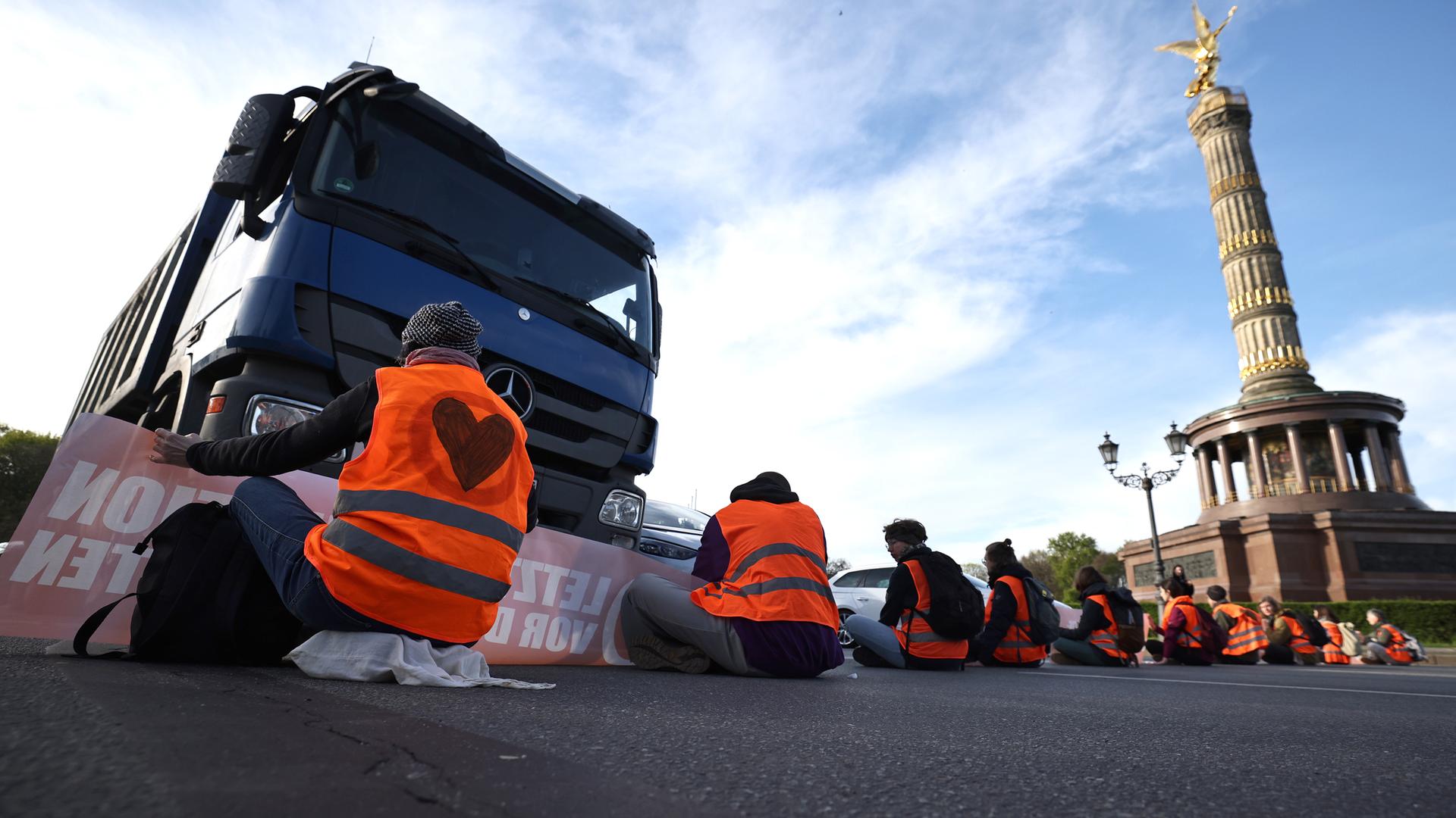 Aktivisten der Letzten Generation sitzen auf der Fahrbahn an der Siegessäule in Berlin und blockieren den Verkehr