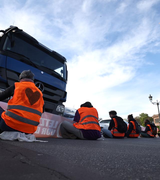 Aktivisten der Letzten Generation sitzen auf der Fahrbahn an der Siegessäule in Berlin und blockieren den Verkehr