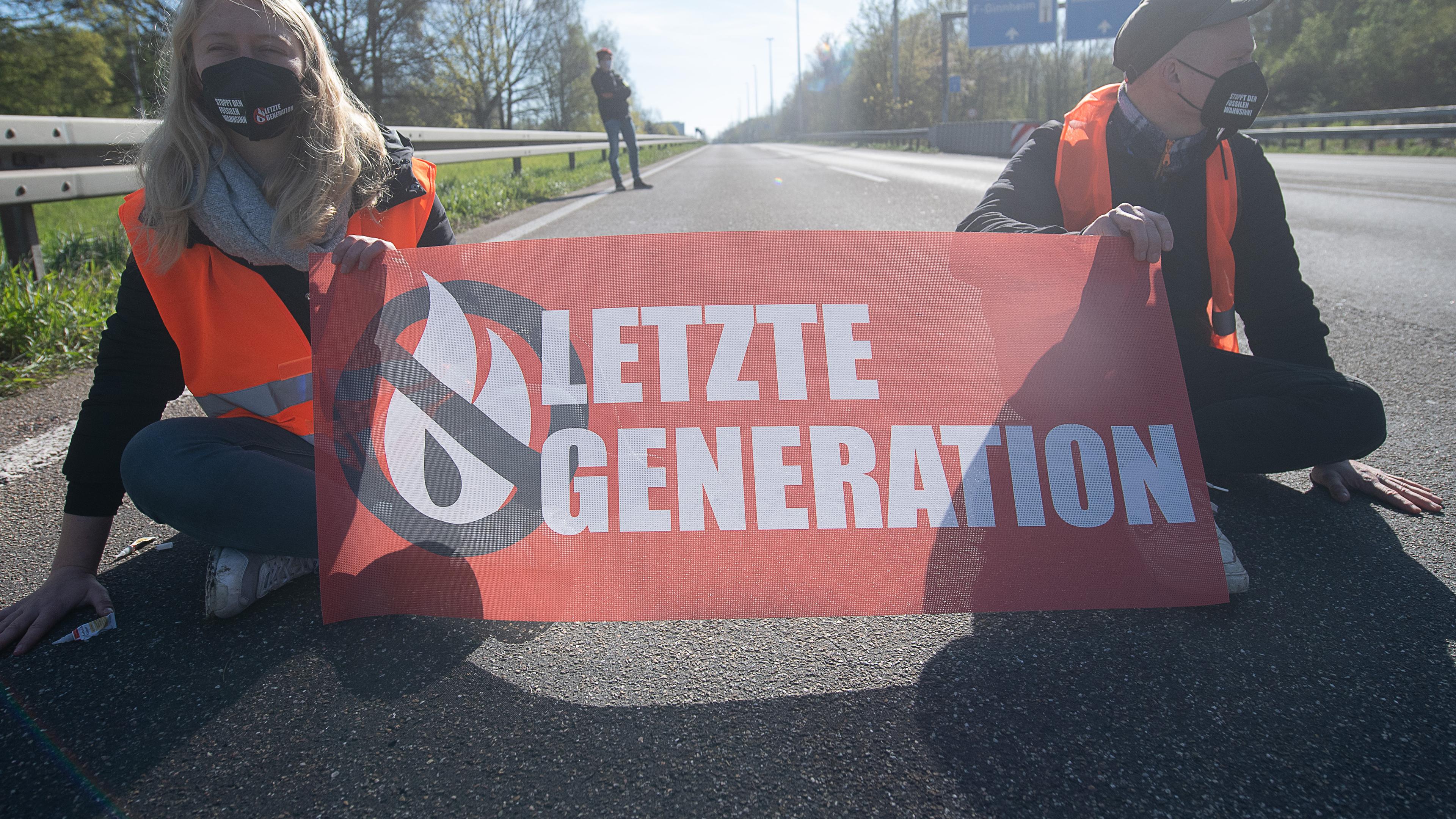 Demonstranten sitzen während einer Blockadeaktion der Protestgruppe "Letzte Generation" auf der A66 mit einem Transparent, auf dem "Letzte Generation" steht.