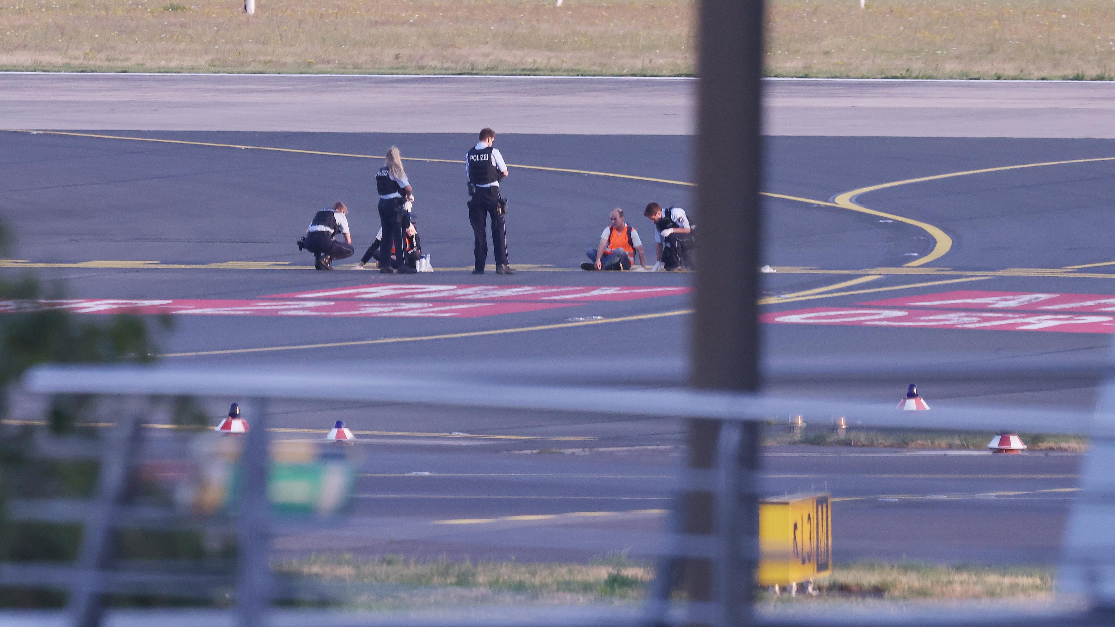 Nordrhein-Westfalen, Düsseldorf: Polizisten stehen auf dem Flugfeld und versuchen Aktivisten der Gruppe Letzte Generation am Flughafen vom Asphalt zu lösen.
