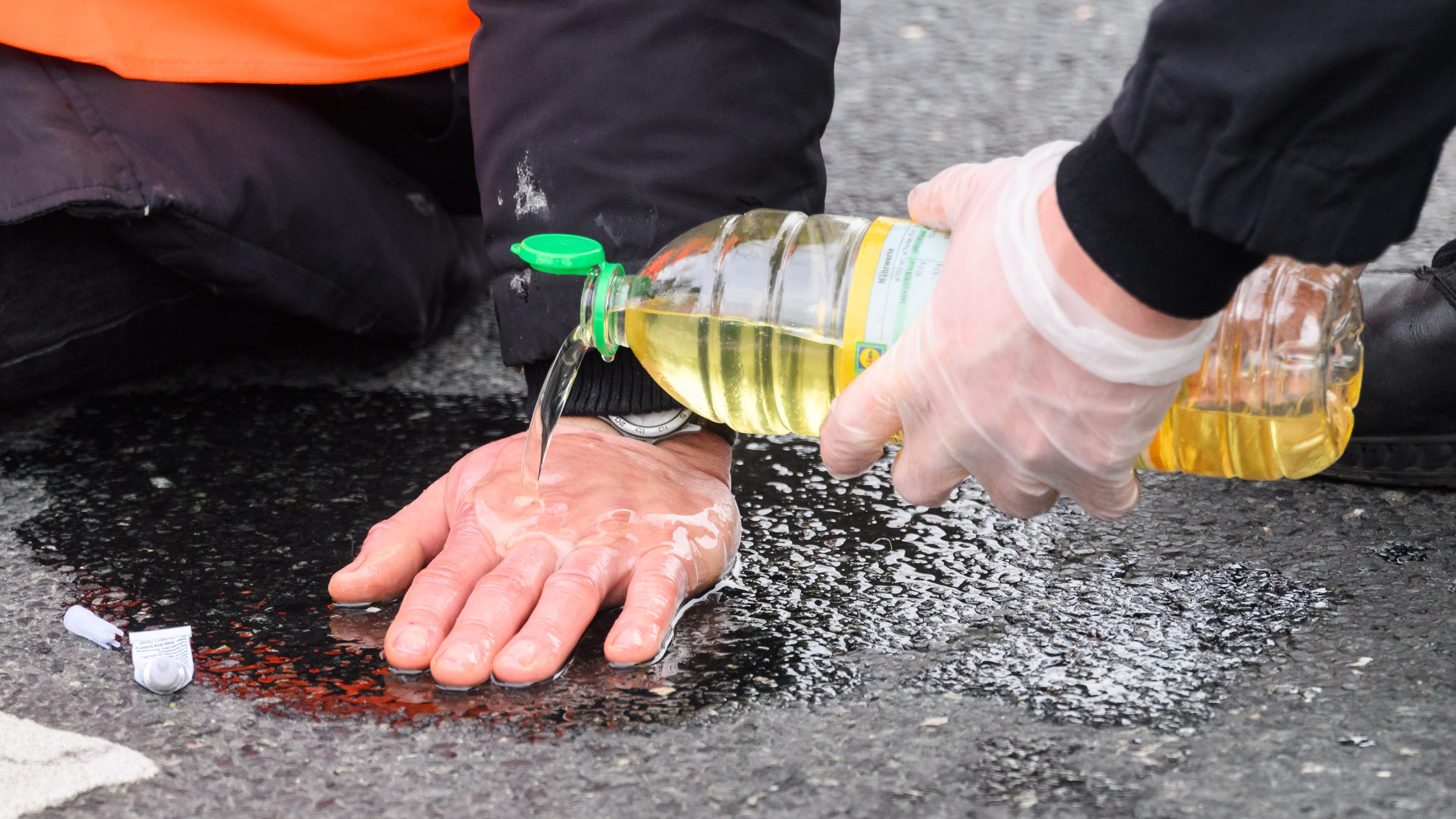 Polizisten versuchen, festgeklebte Hände von Aktivisten der "Letzten Generation" mit Speiseöl von der Straße zu befreien.