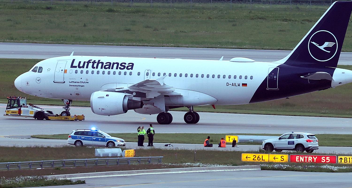 Bayern, München: Zwei Aktivisten haben sich auf einer Zufahrt für Start- und Landebahnen am Flughafen Franz-Josef-Strauß festgeklebt.