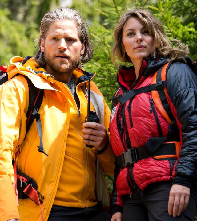 Die Bergretter Markus (Sebastian Ströbel) und Katharina (Luise Bähr) stehen mit ihrer Ausrüstung am Berg. 