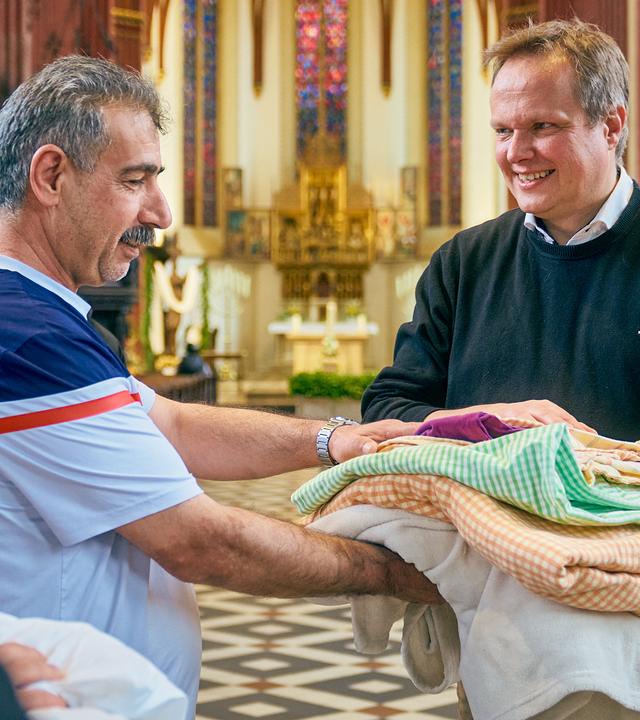 Pfarrer übergibt Decken und Bettwäsche an mehrere Geflüchtete in Kirche.