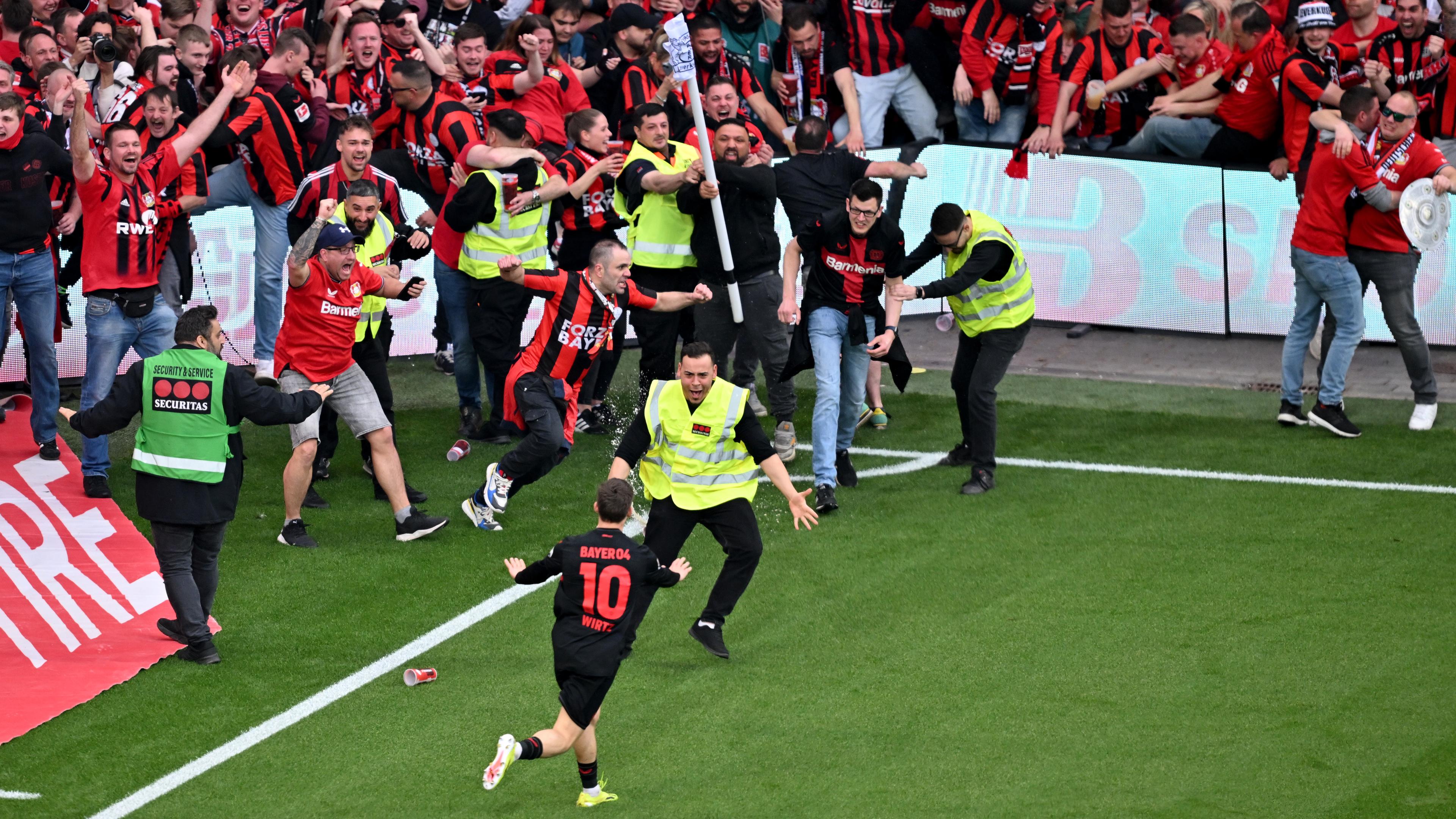 Leverkusens Florian Wirtz dreht nach seinem Tor zum 4:0 jubelnd ab und beruhigt Fans und Sicherheitspersonal, die auf das Spielfeld laufen. 