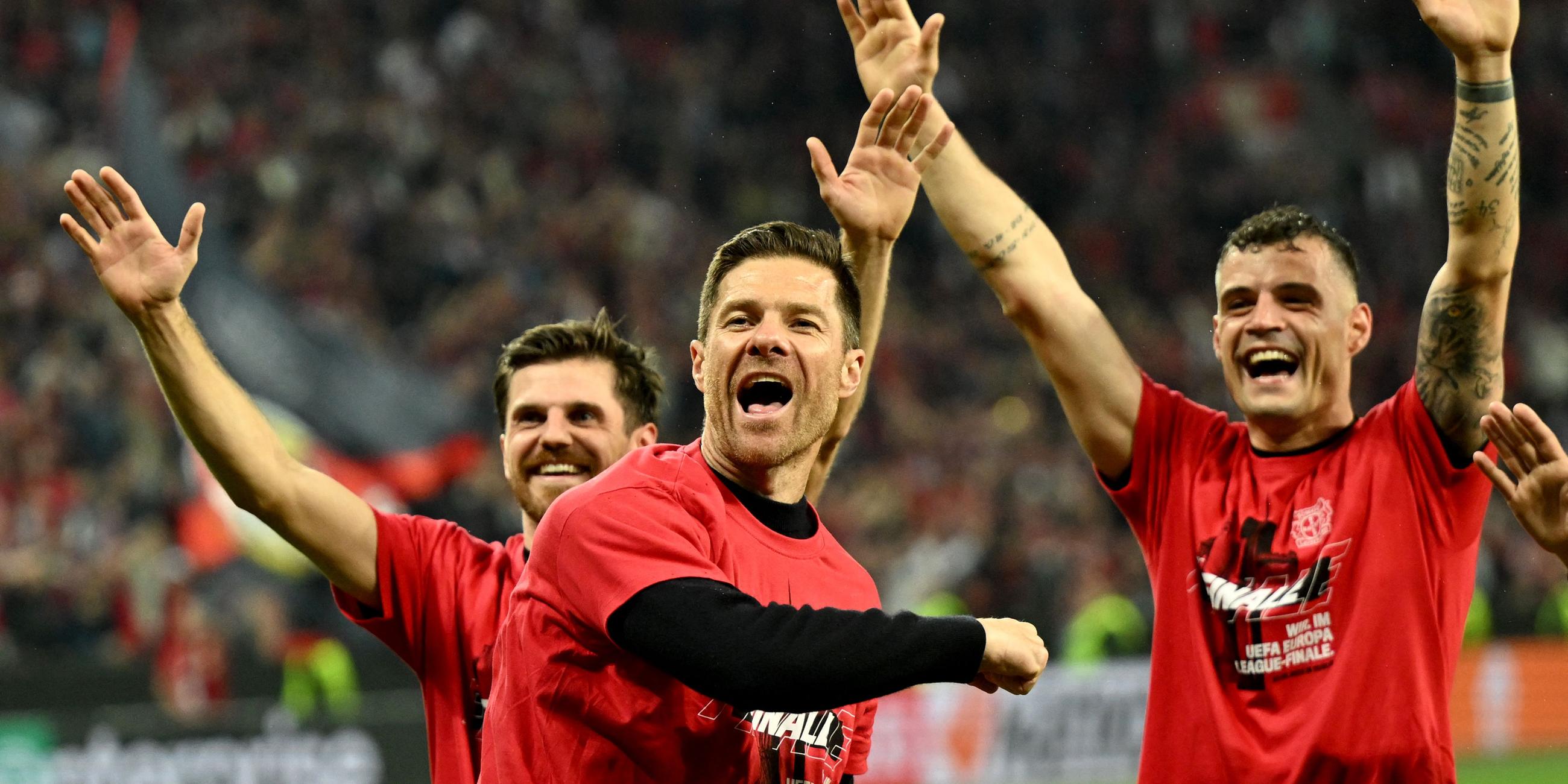 Drei Männer freuen sich auf einem Fußballplatz über den Einzug in Europa-League-Finale. Sie reißen die Arme in den Himmel.