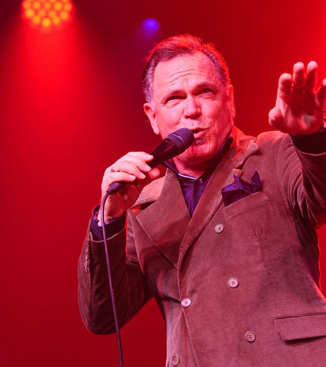 Herr im Anzug und Einstecktuch singt auf einer Bühne