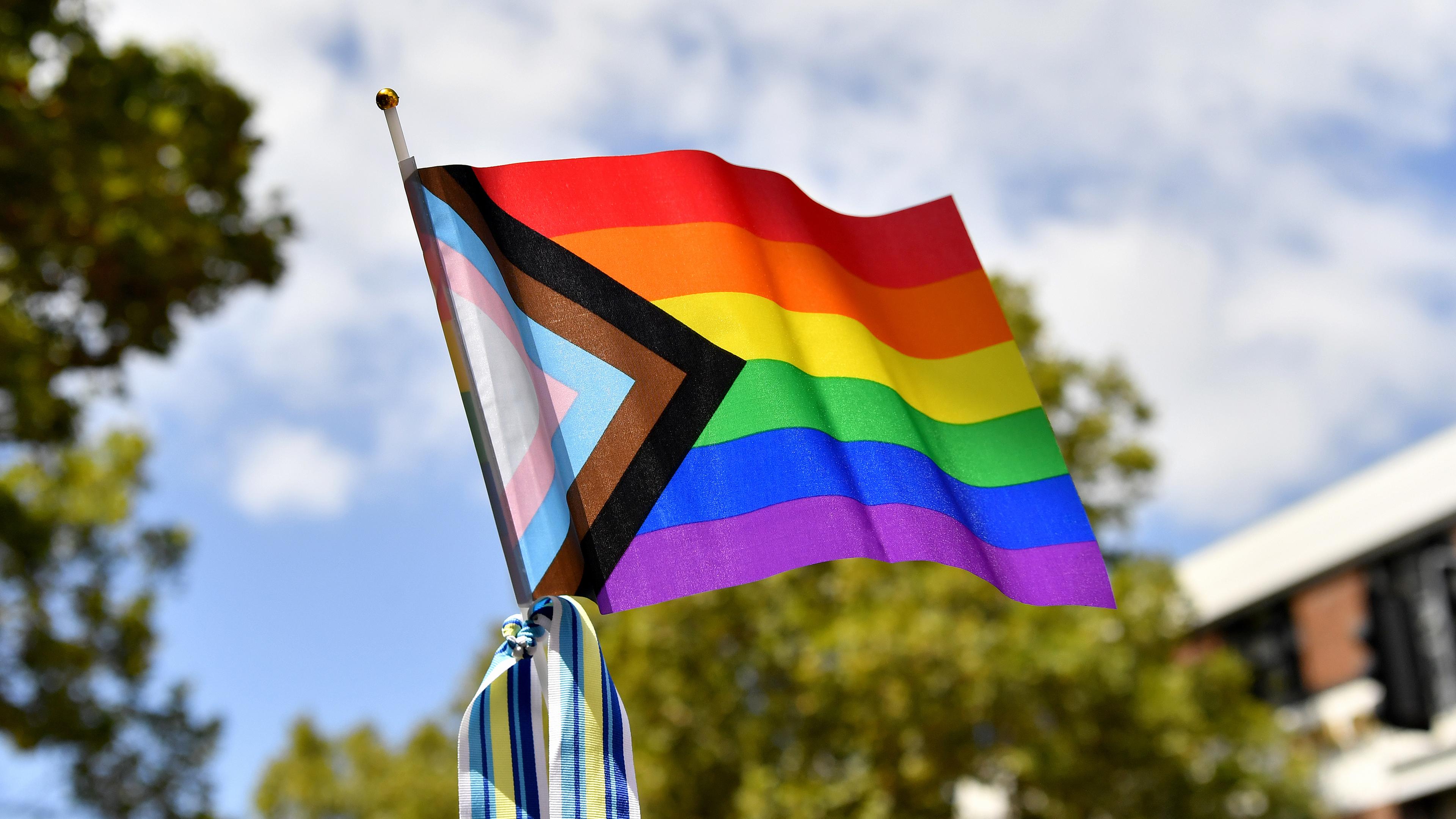 Die Flagge der LGBTQI+-Gemeinschaft wird in die Höhe gehalten.