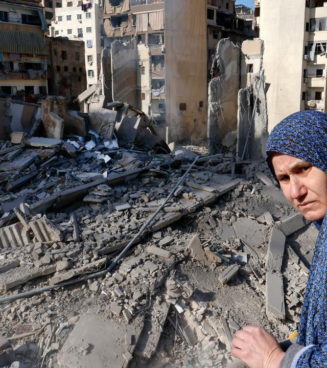 Frau schaut auf Trümmer eines zerstörten Wohnhauses