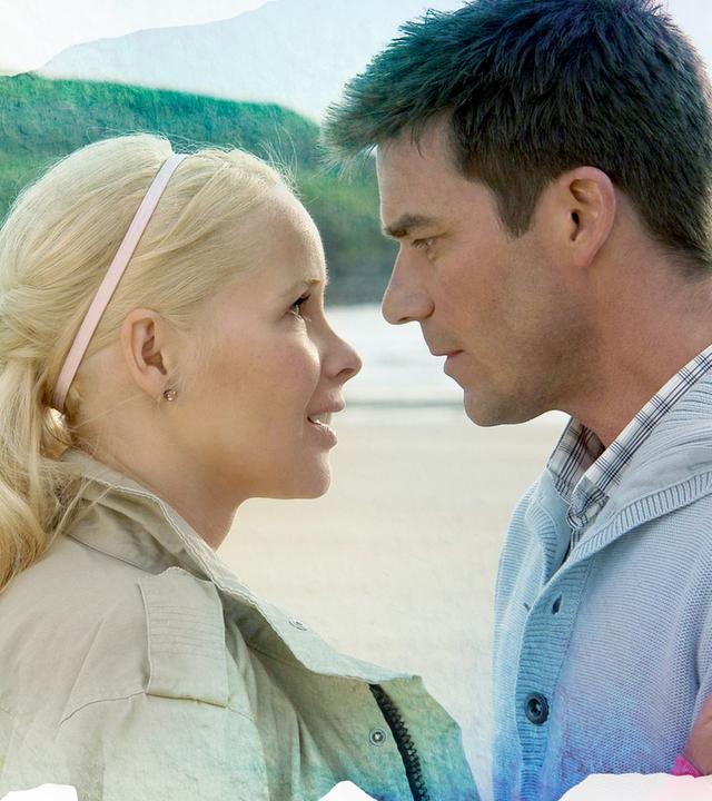 Rachel Wilson (Sylvia Leifheit, links) und Luke Folder (Thomas Scharff, rechts) stehen sich gegenüber und halten sich in den Armen. Ihre Gesichter sind sich sehr nah und sie schauen einander direkt in die Augen.