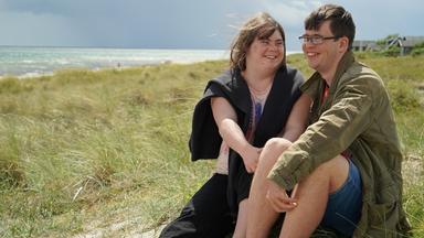 Emily (22) und Erik (22) sitzen auf einer Düne.