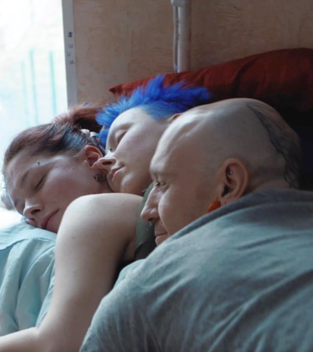 "Liebe und Sex in Russland - Tradition, Gewalt und Widerstand": Ein Mann und zwei Frauen liegen neben einem Fenster aufeinander und schlafen.