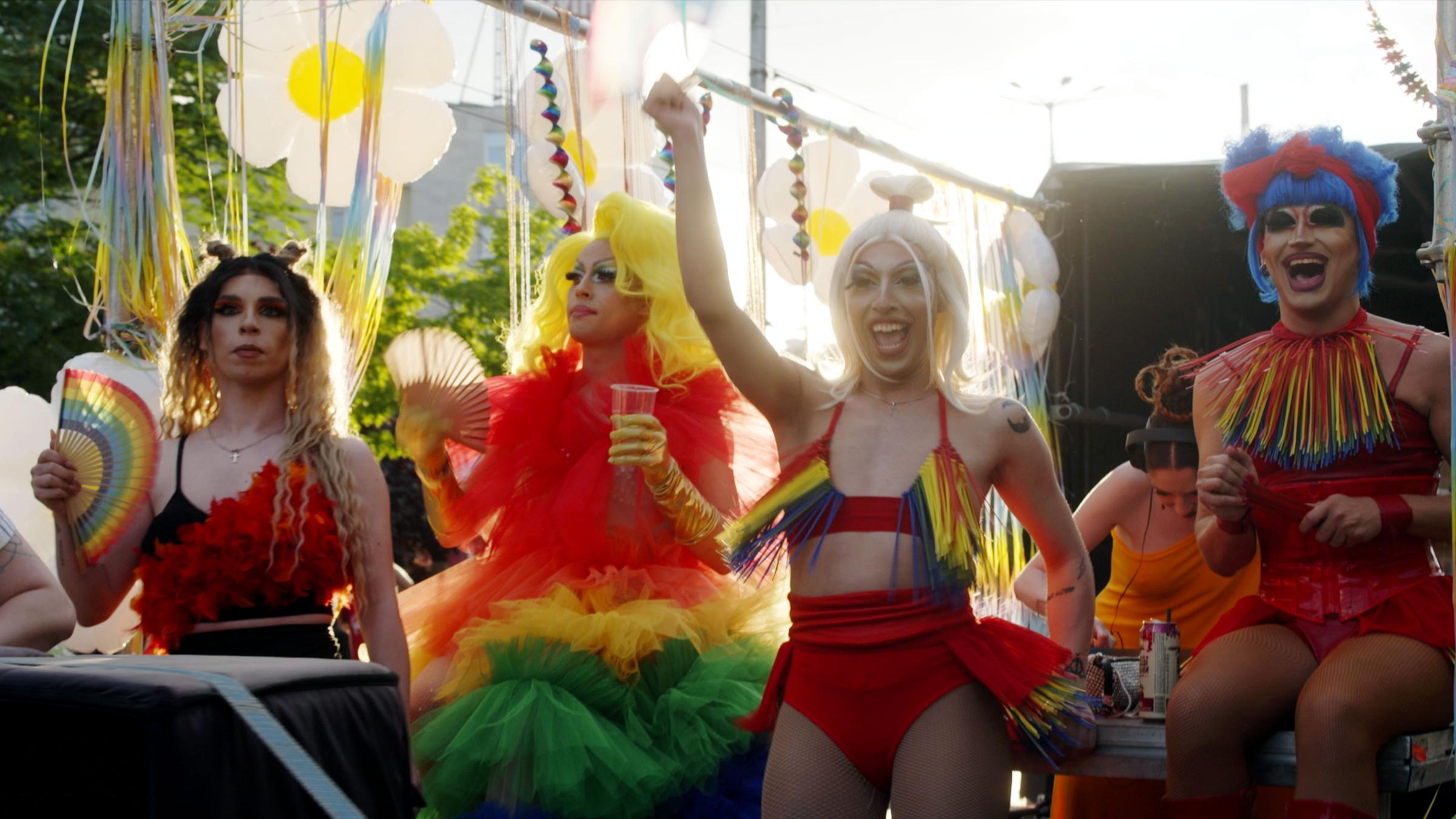 Four transvestites celebrate the Pride Parade on a float.  They wear colorful wigs and costumes.