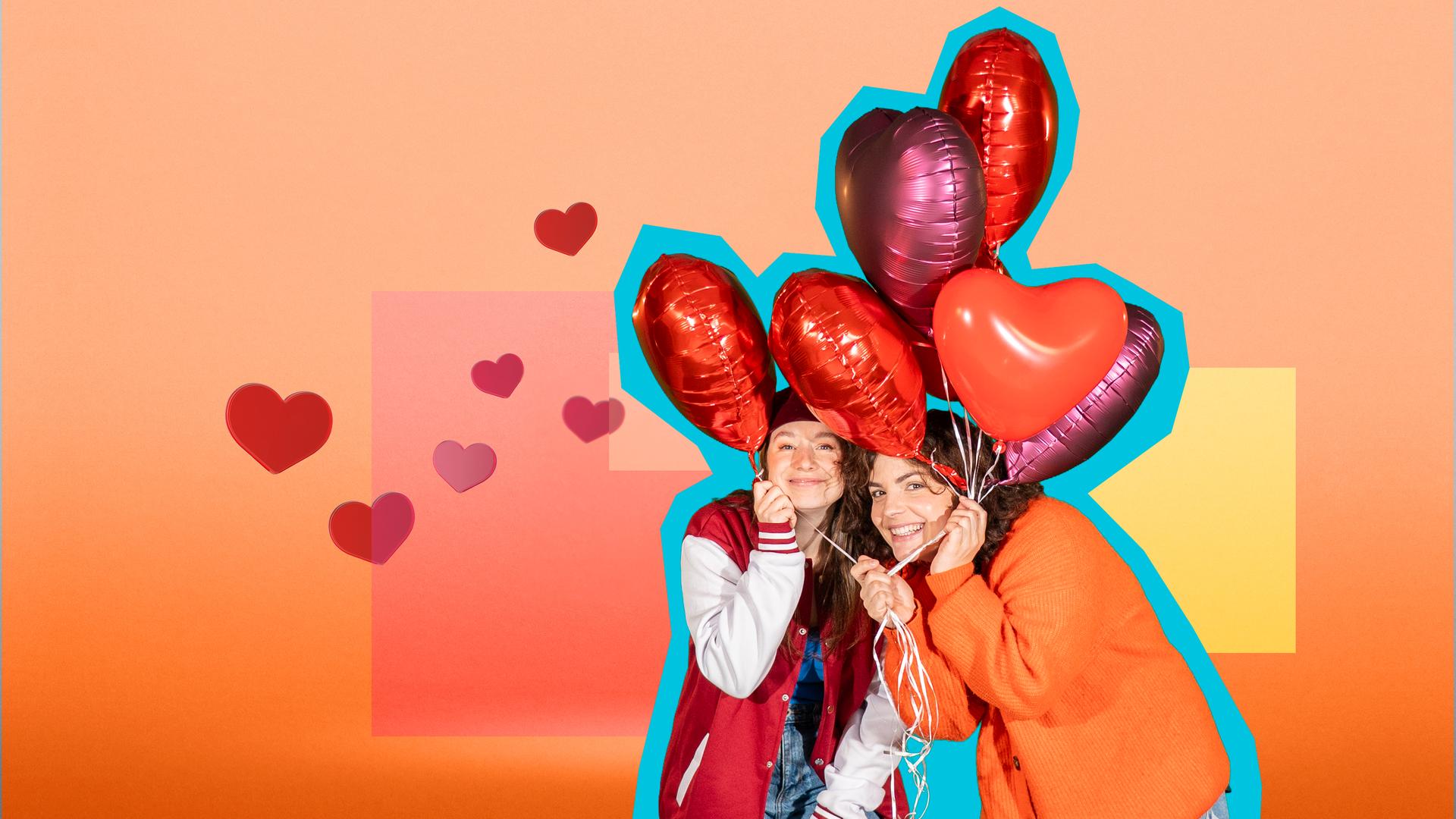 Phela und Senta halten mehrere Herzluftballons in den Händen und lächeln in die Kamera. Der Hintergrund ist gelb-orange-rot.