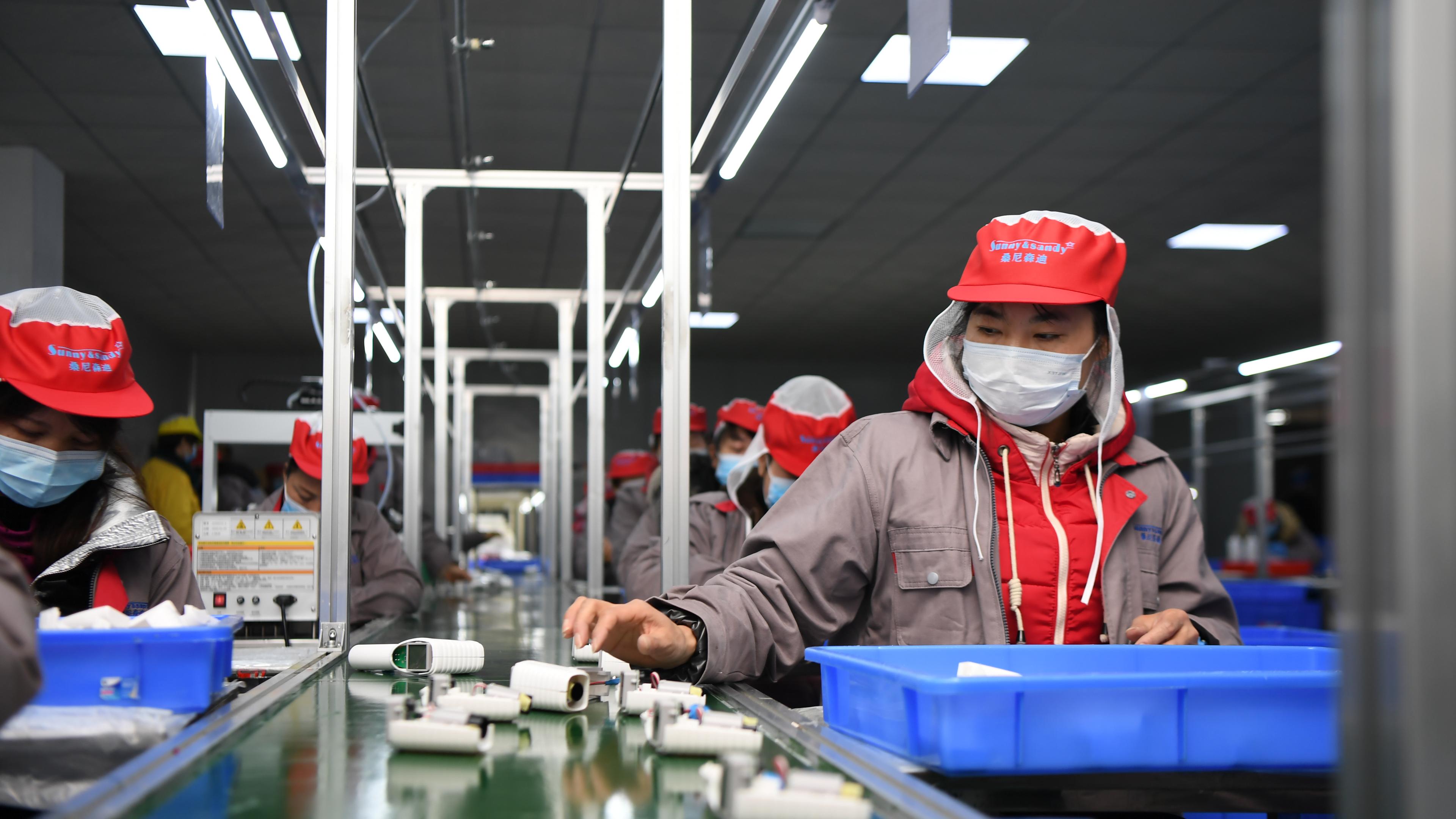 Menschen mit maske arbeiten in einer Fabrik am Fließband