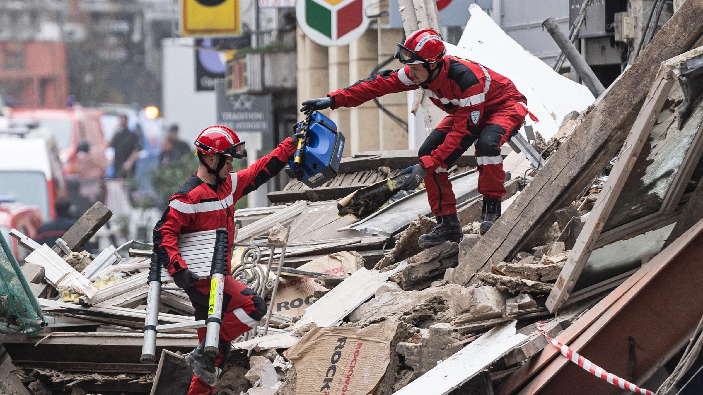 Zwei Rettungskräfte reichen sich Werkzeuge inmitten der Trümmer eines eingestürzten Gebäudes. Lille, Frankreich