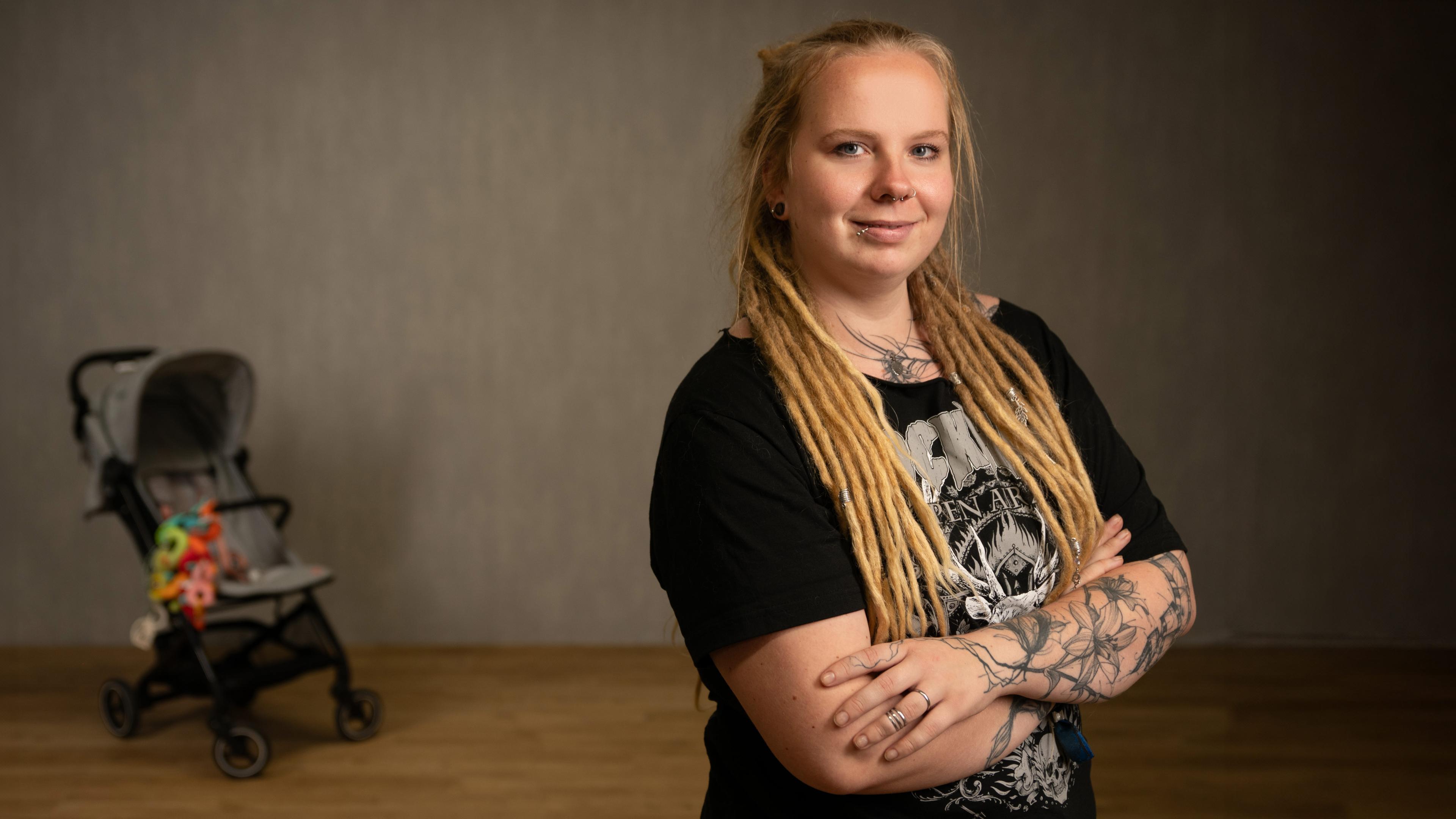 Junge Frau steht neben Kinderwagen und schaut in die Kamera