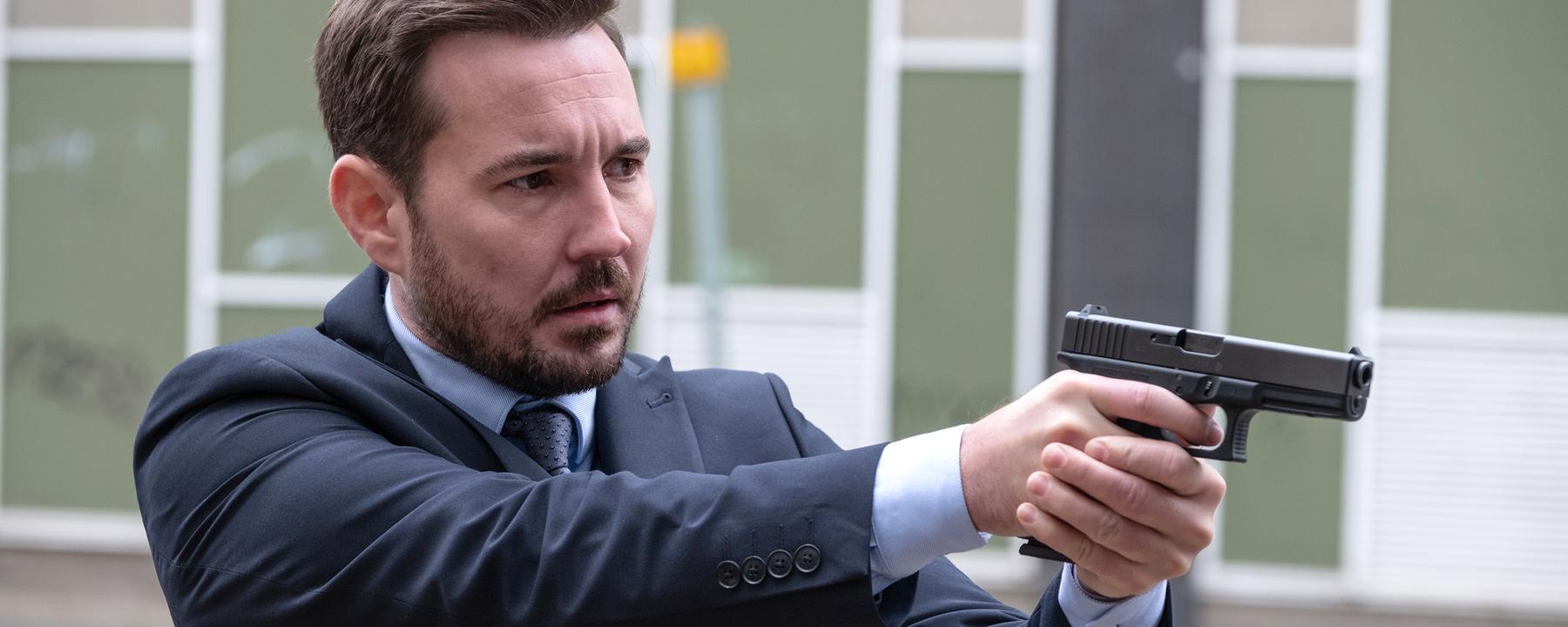 Steve Arnott (Martin Compston) steht im Hinterhof vor einem großen Gebäude und zielt mit seiner Pistole.
