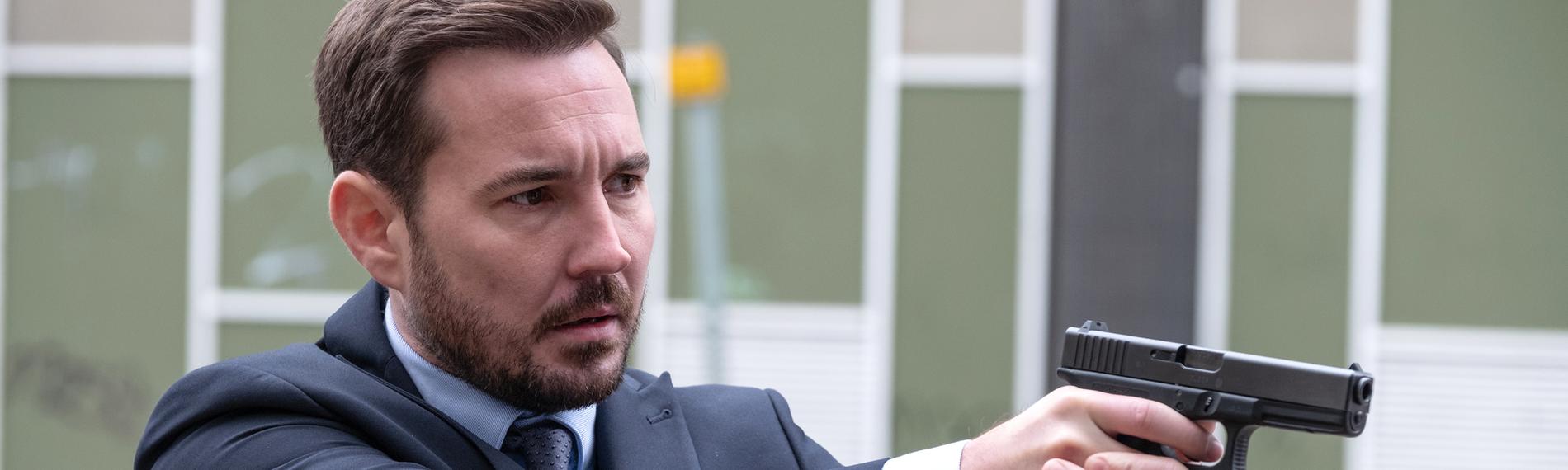 Steve Arnott (Martin Compston) steht im Hinterhof vor einem großen Gebäude und zielt mit seiner Pistole.
