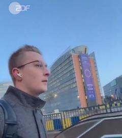 Screenshot ZDF-Volontär Tobias Blum auf Rolltreppe vor dem EU-Gebäude mit EU-Fahne in Brüssel