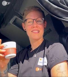 ZDF-Berufskraftfahrerin Nina mit einer ZDF-Kaffeetasse lächelt aus ihrem Fahrerhaus in die Kamera