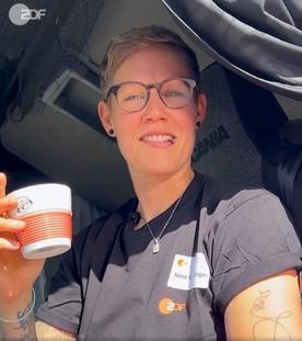 ZDF-Berufskraftfahrerin Nina mit einer ZDF-Kaffeetasse lächelt aus ihrem Fahrerhaus in die Kamera