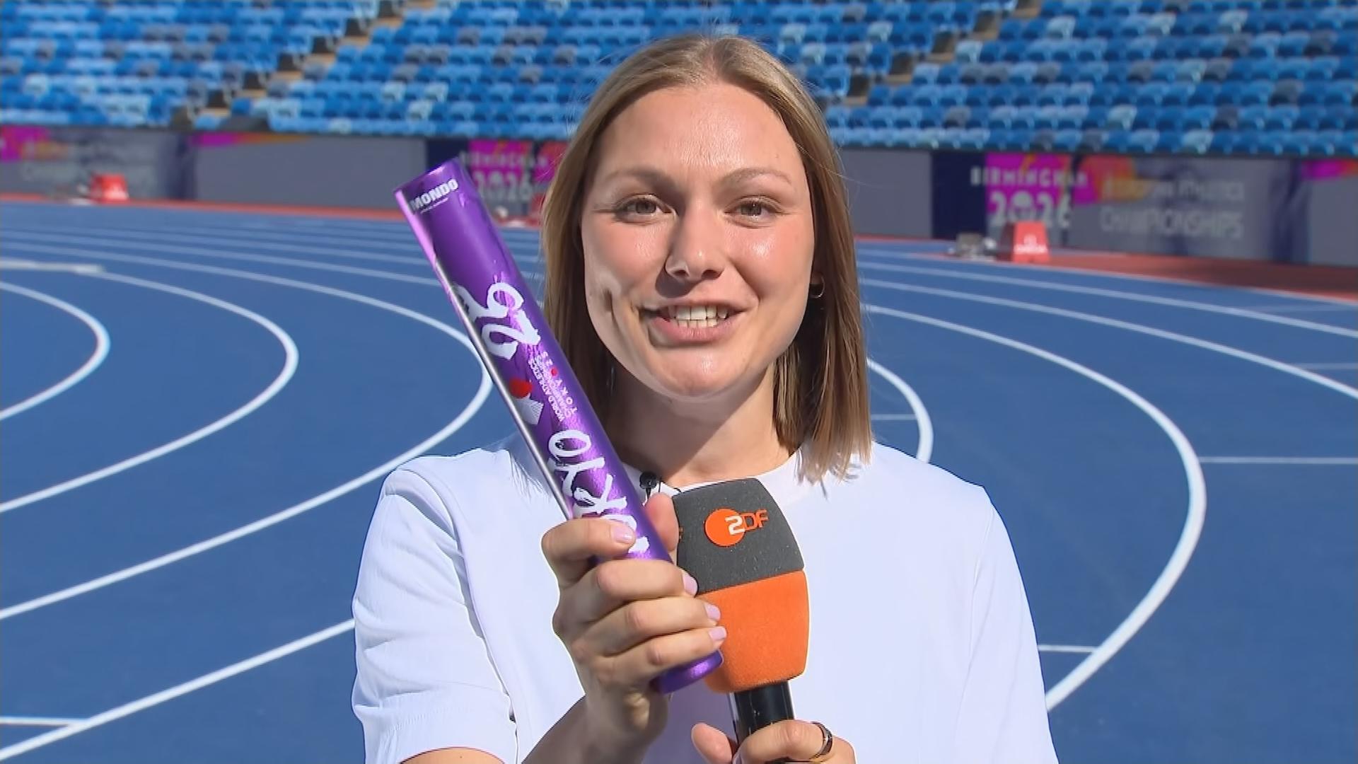 Die ehemalige deutsche Leichtathletin Lisa Mayer hält den Stab, der beim Staffellauf genutzt wird, in die Kamera