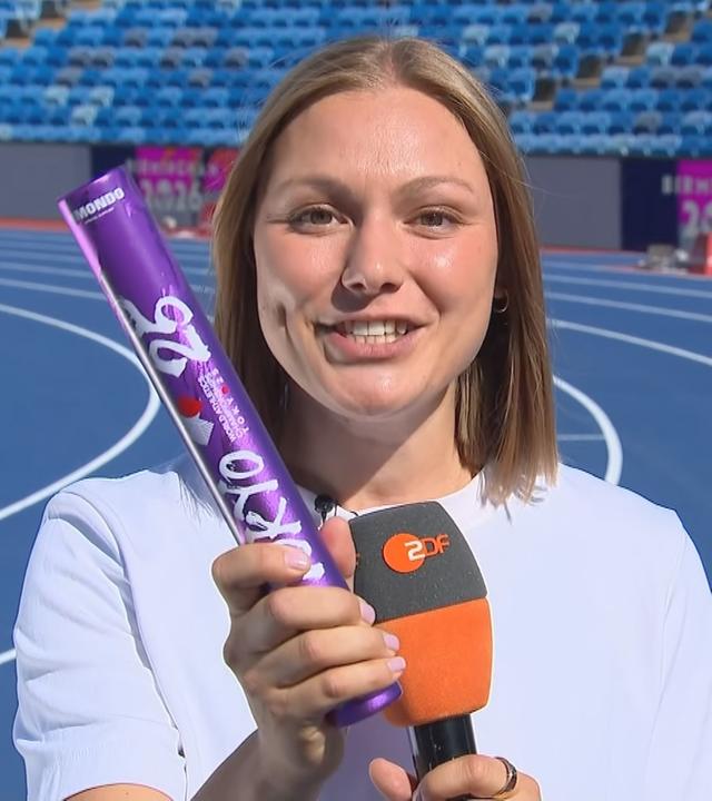 Die ehemalige deutsche Leichtathletin Lisa Mayer hält den Stab, der beim Staffellauf genutzt wird, in die Kamera