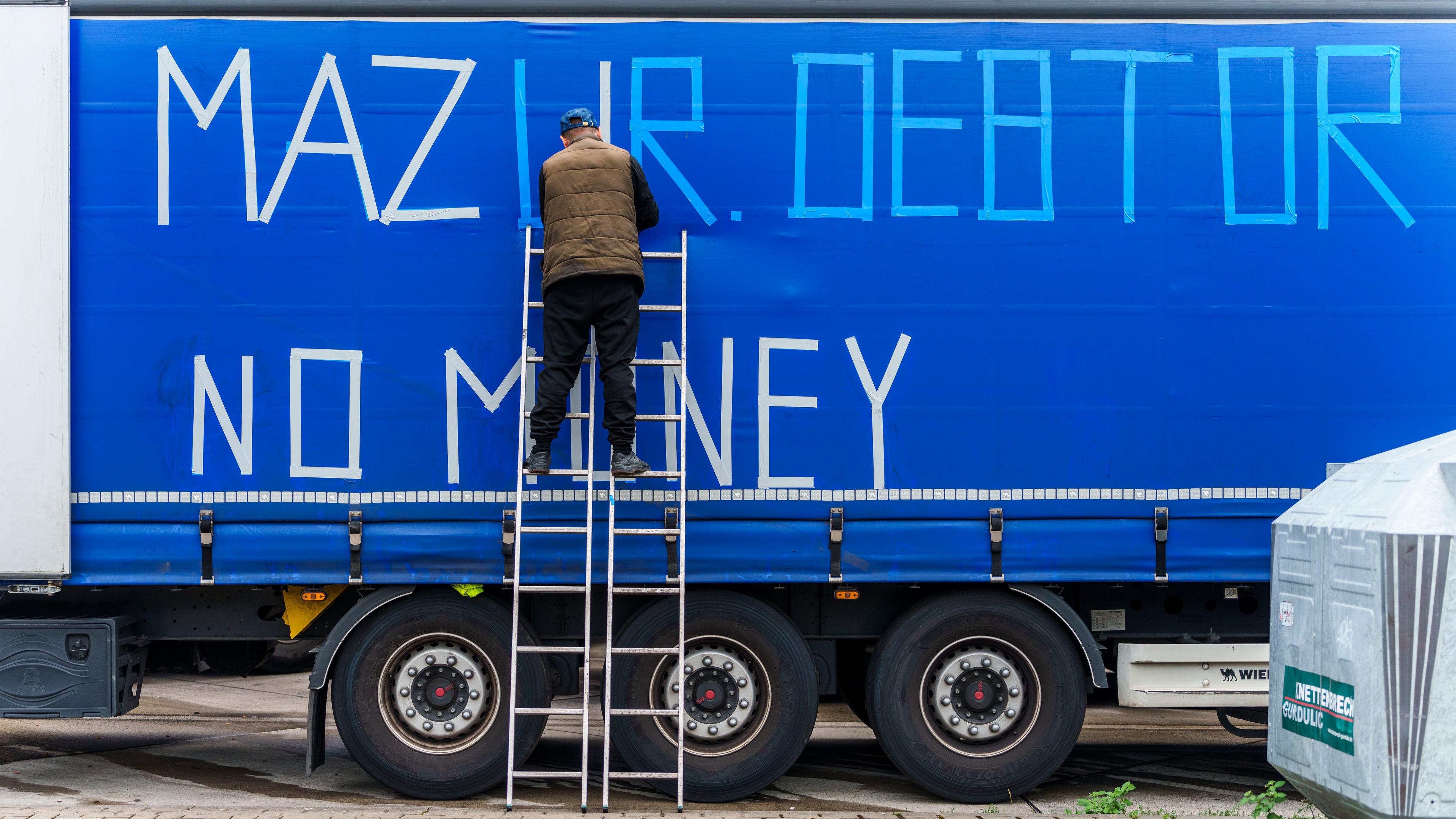 Ein streikender LKW-Fahrer beklebt die Außenplane eines Fahrzeuges ·Mazur Debtor - No Money· an der Raststätte Gräfenhausen.