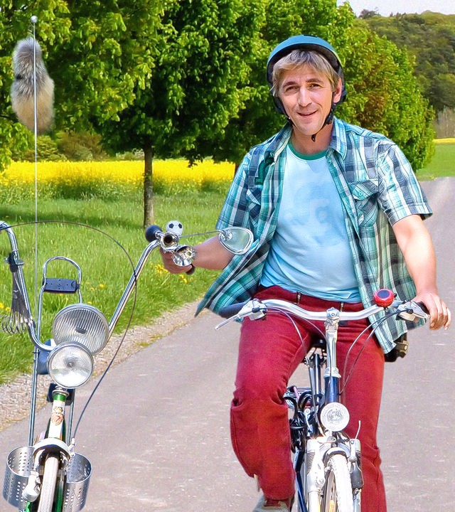 Fritz Fuchs fährt mit einem Fahrrad auf einem Radweg durch blühende Wiesen