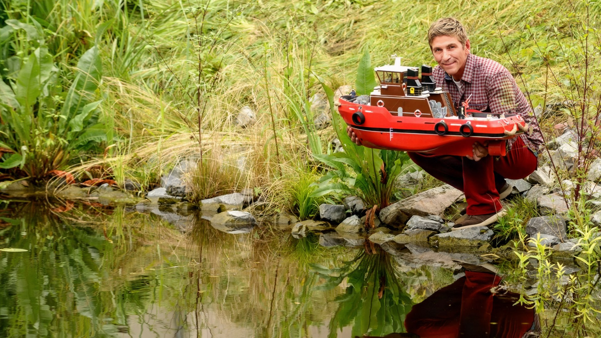 Fritz hockt am Flussufer mit dem Boot Heinz 1 in der Hand.