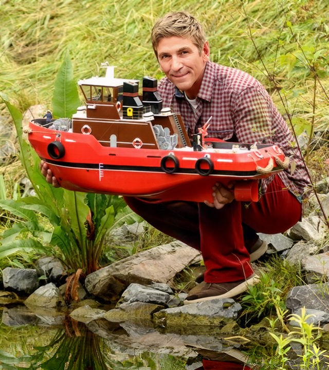 Fritz hockt am Flussufer mit dem Boot Heinz 1 in der Hand.