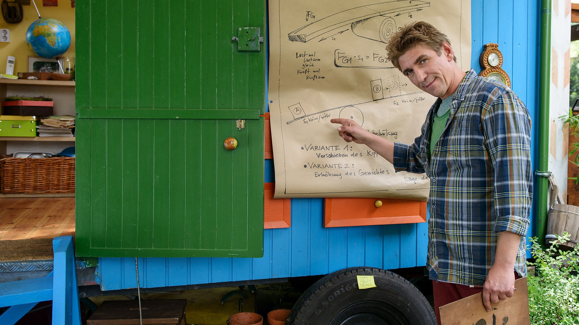 Fritz Fuchs steht vor dem Bauwagen und zeigt auf eine technische Zeichnung