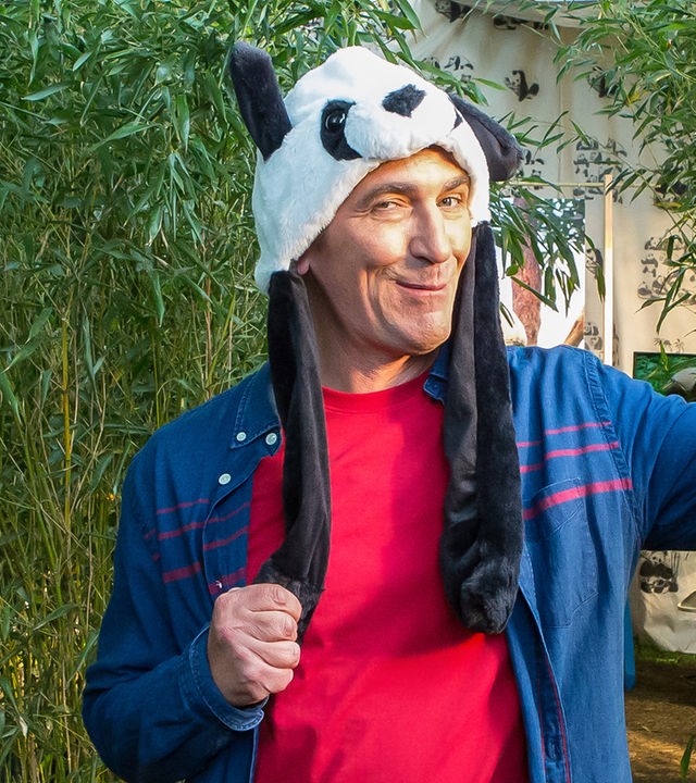 Fritz steht zwischen Kübeln mit Bambus und hat eine Pandamütze auf dem Kopf