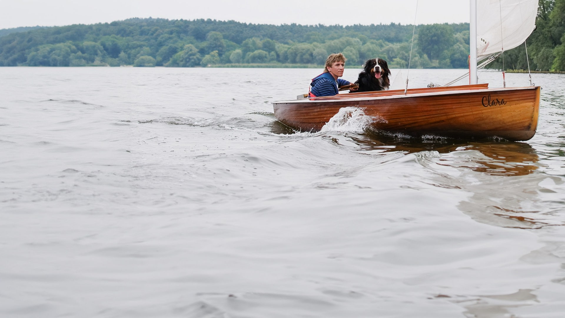 Ein Segelboot mit Fritz und Keks an Bord fährt auf einem See.