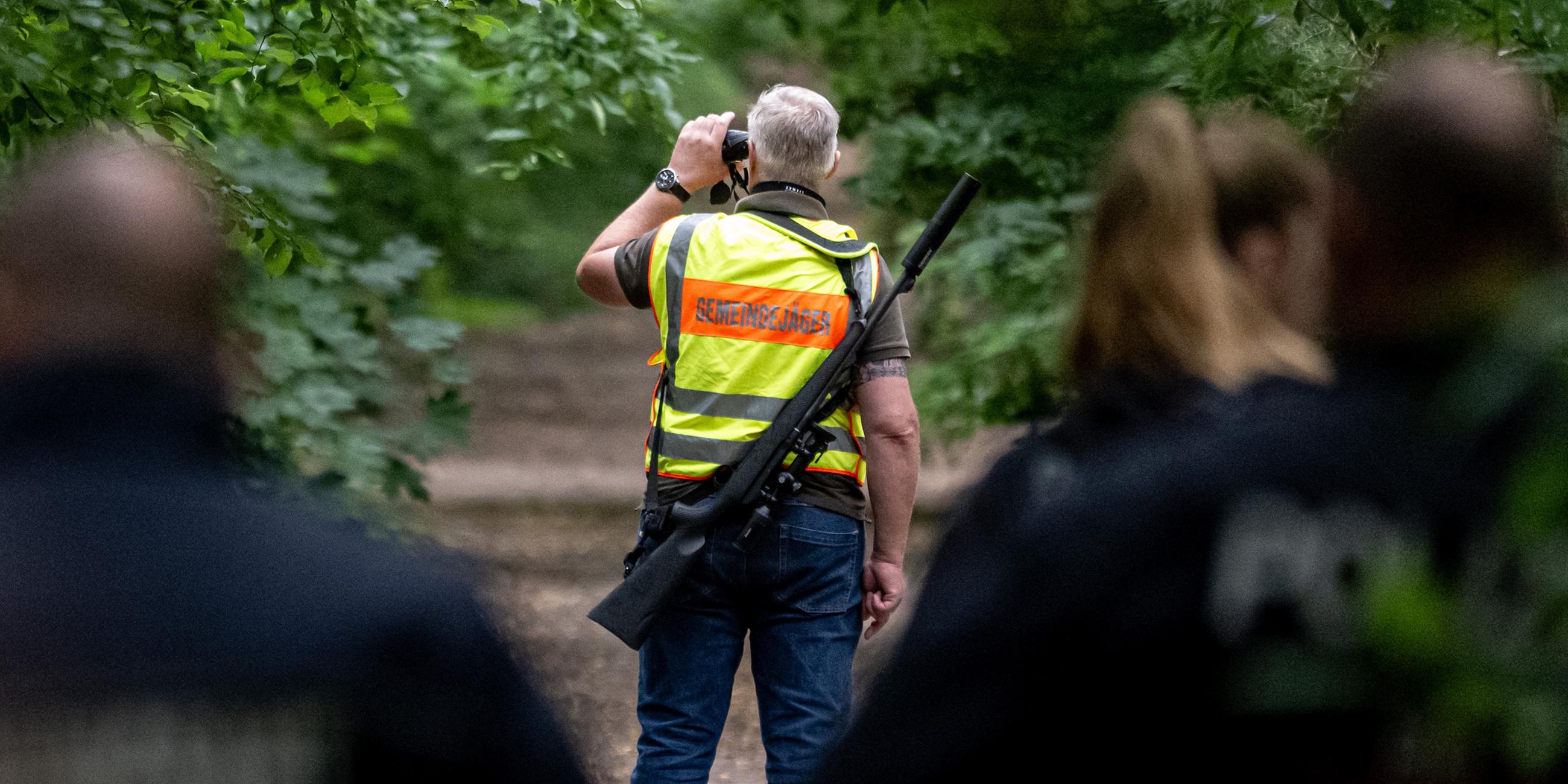 Der Gemeindejäger (M) und ein Mitarbeiter Ordnungsamt durchsuchen im Bereich der südlichen Landesgrenze von Berlin den Wald.
