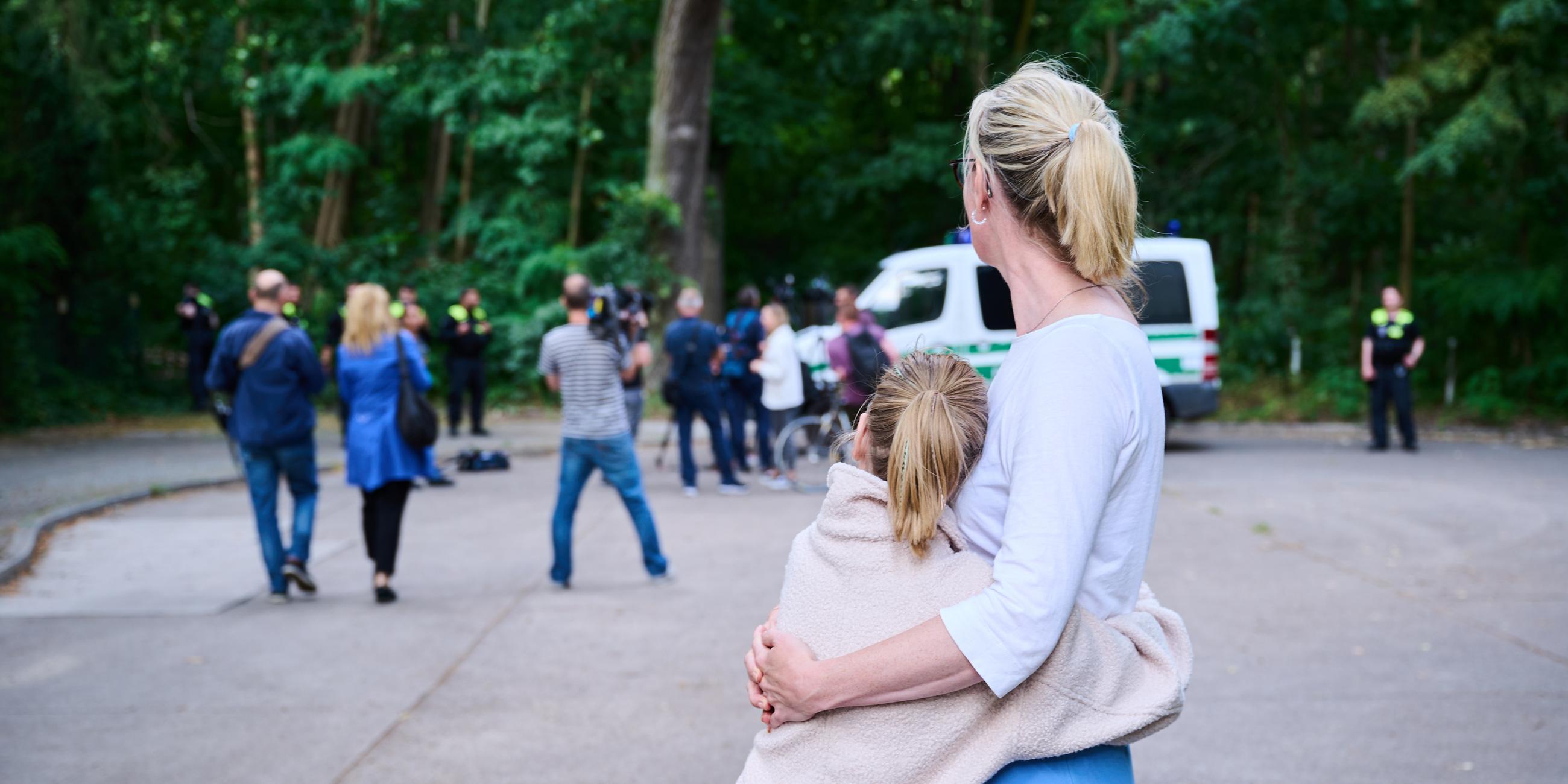 Eine Anwohnerin und ihre Tochter sehen dem Treiben von Journalisten und Polizei zu, während Tierexperten und Polizeibeamten in einem Waldgebiet in Zehlendorf stehen. 