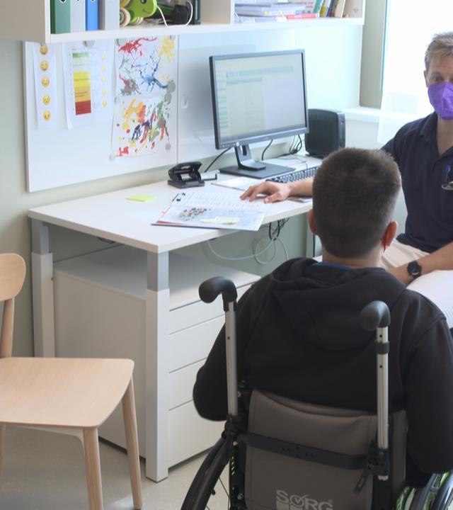 Junge im Rollstuhl spricht mit Kinderarzt