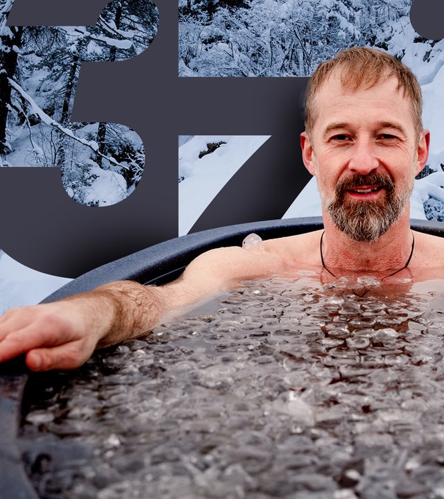 Ein Mann im Schneidersitz sitzt nur mit Badehose und Mütze bekleidet im Schnee in den Bergen.