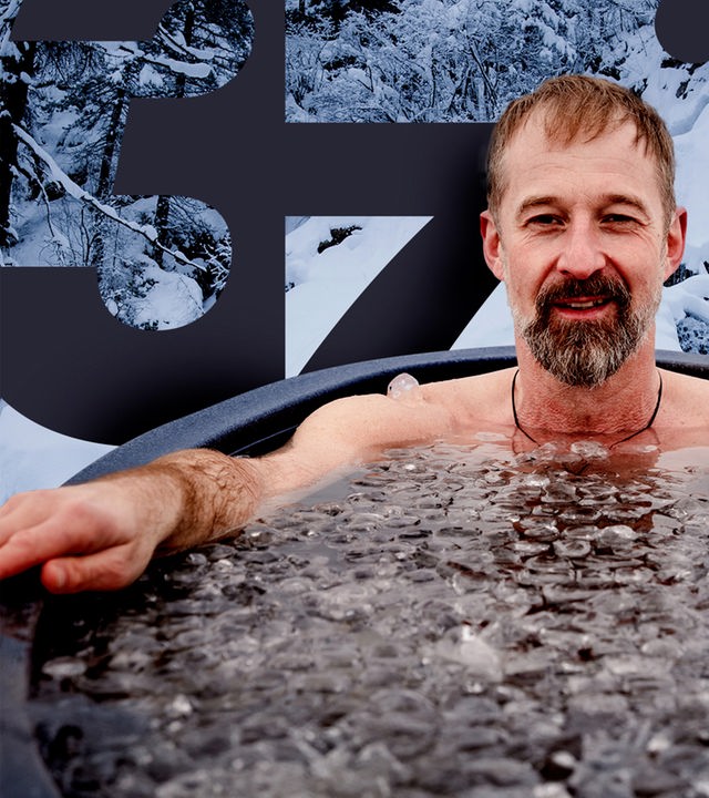 Ein Mann im Schneidersitz sitzt nur mit Badehose und Mütze bekleidet im Schnee in den Bergen.